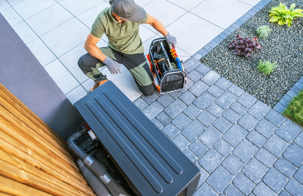 A,technician,kneels,beside,an,outdoor,hvac,unit,,carefully,organizing